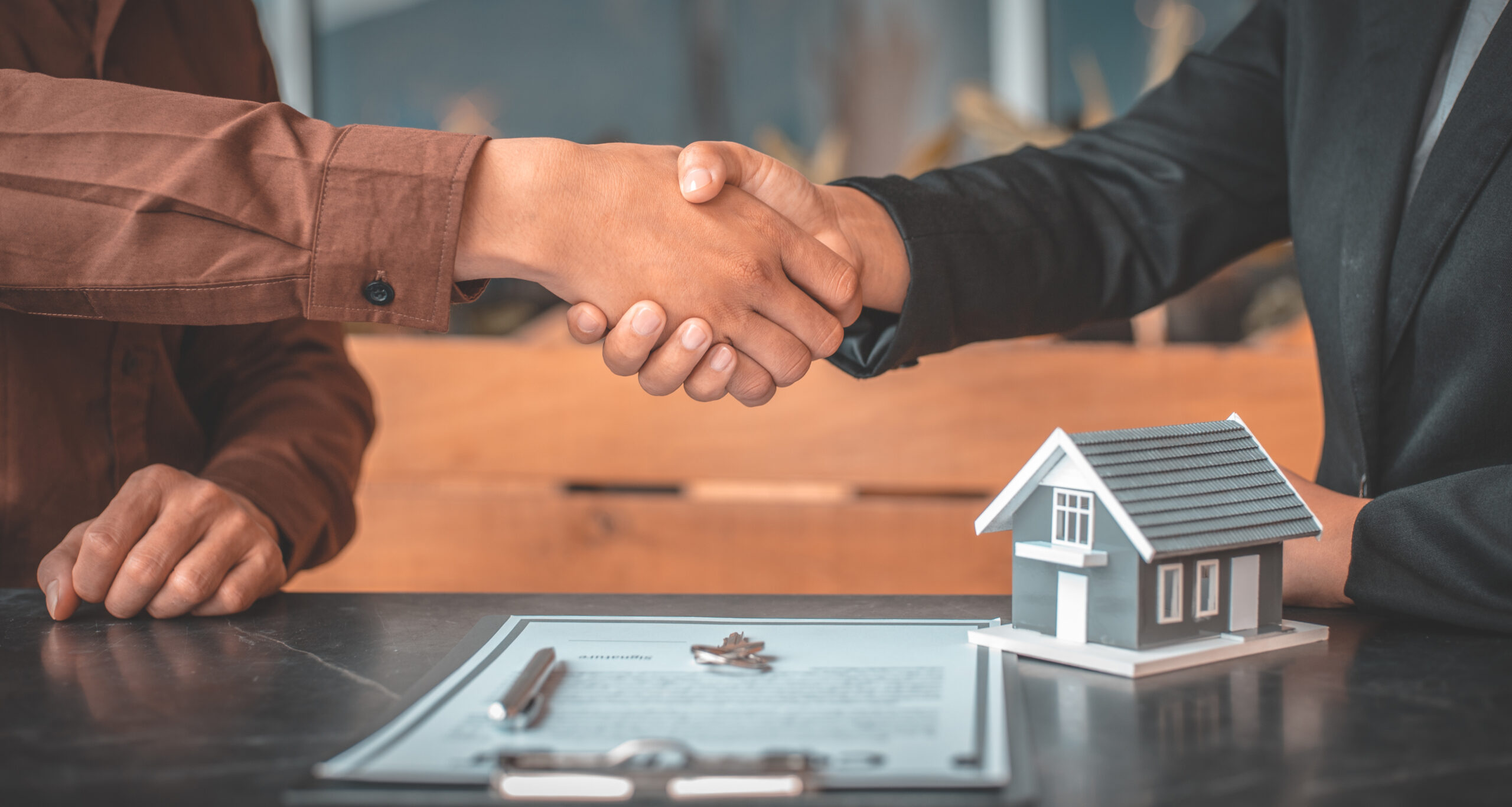 Two people shaking hands over a real estate agreement.